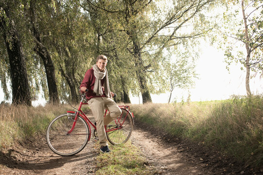 Cyclist standing with bicycle on wooded lane in autumn