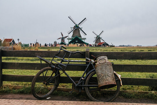 Rustic bicycle carrying an antique milk churn on a wooden fence, overlooking the iconic historic windmills and traditional dutch houses in zaanse schans landscape