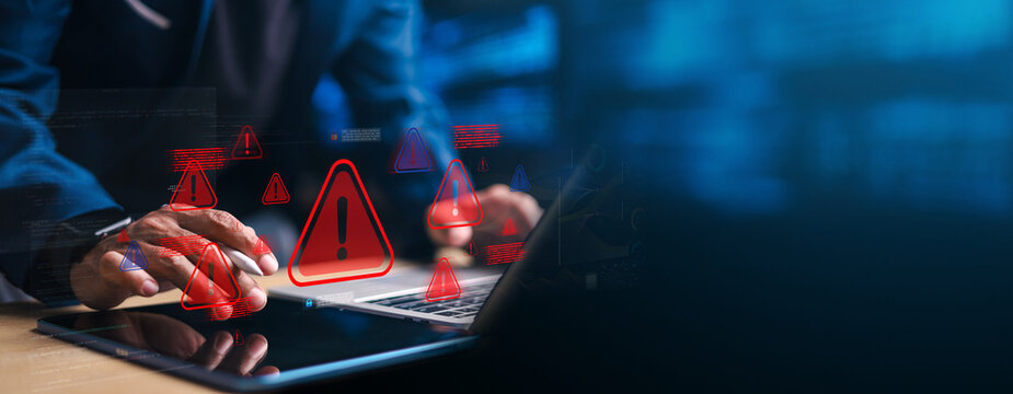 Business professional using laptop with red warning alert icons hologram interface. Concept of cybersecurity threat, data breach, malware attack, system risk and online protection.