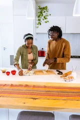 Fotobehang Koken African American couple in casual clothes preparing pastry in bright kitchen, using eggs and milk  © wavebreak3