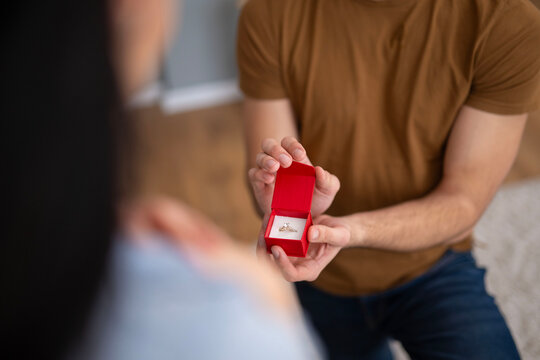 Man proposing marriage holding engagement ring in red box