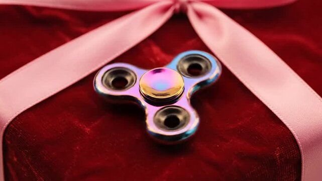 Iridescent fidget spinner spinning on a red velvet surface with a pink ribbon bow