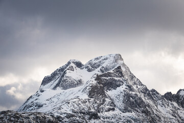 Obraz premium Glowing Arctic light cuts through the clouds and highlights the sharp snowy peaks around Sund, Lofoten, Norway, revealing the raw power of the northern mountain