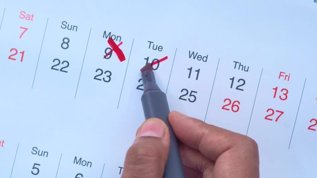 Close up video showing a hand marking off dates on a calendar with a red marker, indicating progress or completion of tasks