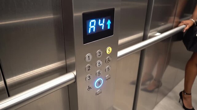 Woman presses fifth floor button inside modern stainless steel elevator