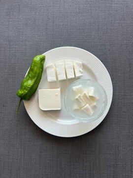 Slices of Turkish white cheese (feta) with green pepper.

A clean presentation of sliced white brined cheese (feta) served on a white plate with a fresh green pepper on the side, a staple