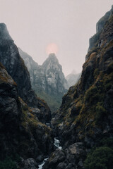 Obraz premium Dramatic Mountain Canyon with Misty Peaks and Soft Sun Glowing over Steep Rocky Cliffs and River