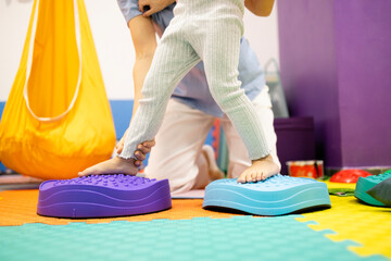 Fototapeta na wymiar Pediatric physiatrist supporting a child balancing on sensory stepping stones during a physical therapy session for rehabilitation and developmental coordination