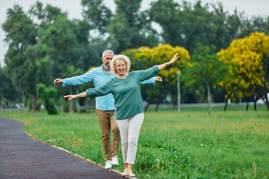 Happy active mid aged adult couple having fun walking and balancing and bonding in park or nature outdoors, healhty active mature people exercise concept