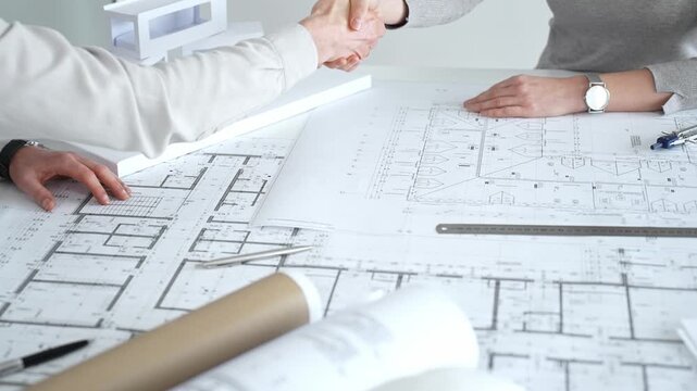 Handshaking between two architects finalizing a construction project deal, business partners agreeing on engineering blueprints and architectural models in an office, close up