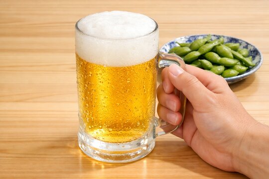 居酒屋の木目調テーブルで冷えた生ビールジョッキを手に持ち枝豆と一緒に楽しむ男性