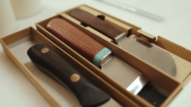 Close up of leather crafting tools arranged in box inside artisan workshop. Wooden handle knives and cutting tools reflect handmade production and small batch craftsmanship environment.