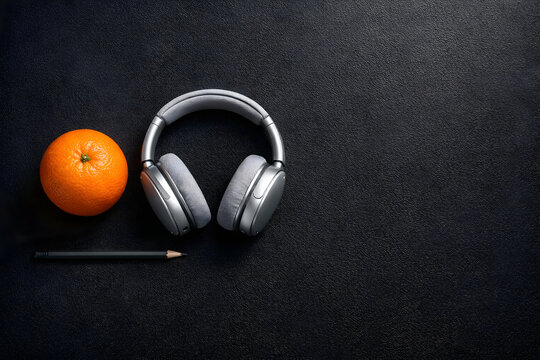 Buah jeruk bersama headphone dan pensil di atas meja hitam melambangkan keseimbangan antara pekerjaan kreatif dan gaya hidup sehat