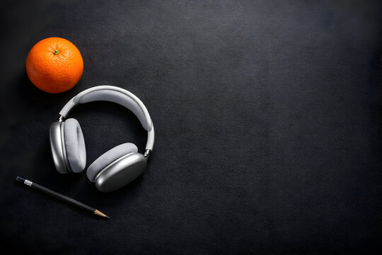 Headphone nirkabel dengan buah jeruk dan pensil di latar belakang gelap melambangkan jeda istirahat produktif dan konsumsi camilan sehat