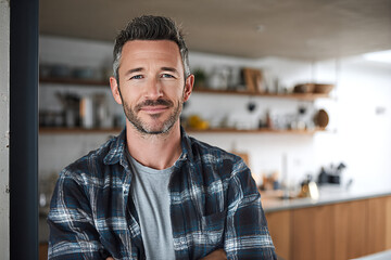 Obraz premium Middle - aged homeowner with salt - and - pepper stubble smiling, arms crossed and leaning on doorway in blue plaid shirt, direct eye contact in bright modern kitchen lit by soft natural light