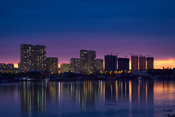 Fototapeta premium Night cityscape of Heihe with illuminated high‑rises and cranes over the waterfront skyline