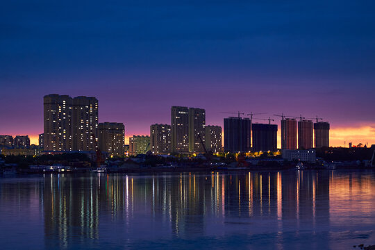 Night cityscape of Heihe with illuminated high‑rises and cranes over the waterfront skyline