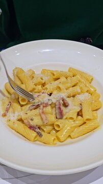 Delicious plate of pasta Carbonara with rigatoni, guanciale, egg yolk, pecorino cheese and black pepper, typical Roman recipe eaten in a restaurant, representing Italian culinary traditions