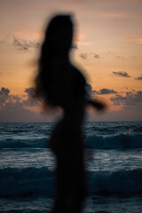 Fototapeta premium Silhouette of a Woman Standing on the Beach Enjoying Ocean Waves During a Beautiful Tropical Sunset in Sri Lanka