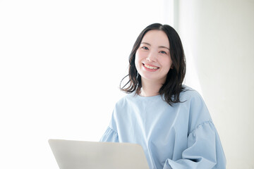 明るい部屋でパソコンで仕事や検索、調べるお洒落な女性　資格や勉強などのスキルアップ、キャリアアップの前向きなポジティブイメージカメラ目線