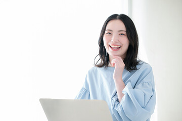 明るい部屋でパソコンで仕事や検索、調べるお洒落な女性　資格や勉強などのスキルアップ、キャリアアップの前向きなポジティブイメージカメラ目線で顎に手を当てる考える