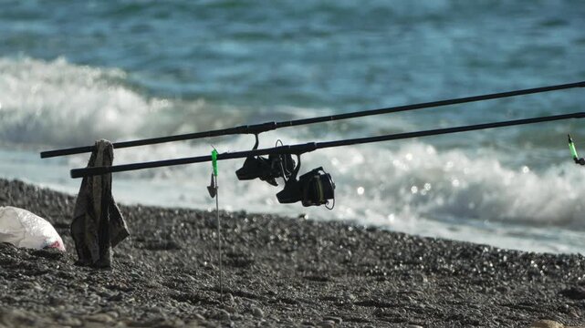 Fishing rods coastline wait for catch on Mediterranean rocky beach during bright sunny day.