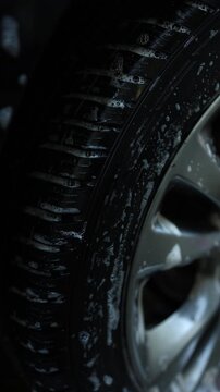 Cleaning car wheel with soap and water in a backyard during a sunny afternoon The suds are visible on the shiny rim.
