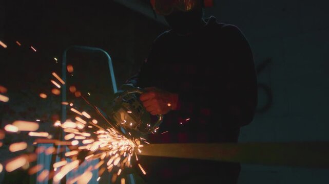 Man working at factory cuts metal with a grinder. Male at a construction site cuts off piece, bright flying sparks and particles of material fly. Guy Industrial worker use angle grinder cutting metal