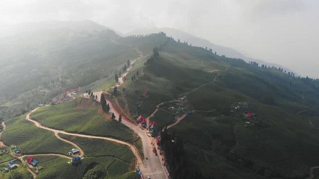 Drone view of lush green tea plantations / Tea gardwn in Ilam, eastern Nepal, with rolling hills, misty mountains, and small red roof houses surrounded by nature.