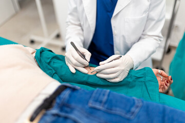 Close-up of doctor removing mole from patient arm with surgical tweezers and scalpel. Dermatology...