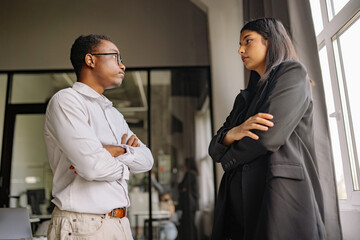 Two colleagues engaging in a serious discussion inside a modern office setting during daylight hours © yaaaaan