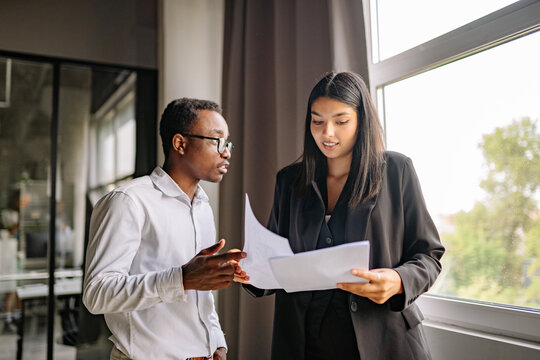 Black man discusses a contract with a woman in a modern office space during daytime
