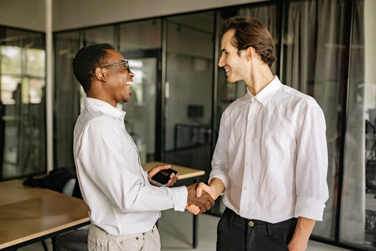 Two professionals shaking hands in a modern office setting during a business meeting on a sunny day, showcasing collaboration and mutual respect