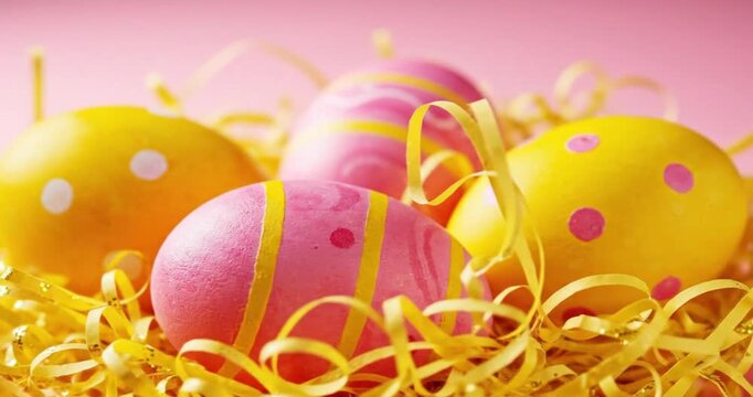 A captivating close-up showcases a collection of vibrantly decorated eggs, artfully nestled amidst a shimmering bed of yellow shredded decorative paper. The eggs feature cheerful pink and sunny yellow