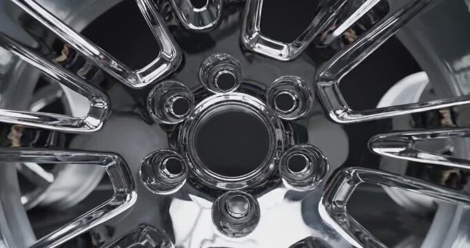 A captivating close-up showcases the intricate design of a highly polished, chrome-plated automotive wheel. The metallic surface gleams and reflects ambient light, highlighting the sleek curves and de