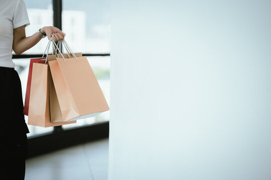 Young woman holding colorful shopping bags while checking her smartphone in a modern mall, lifestyle consumer concept with copy space.