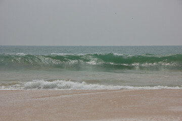 Ocean wave breaking on sandy beach under gray sky