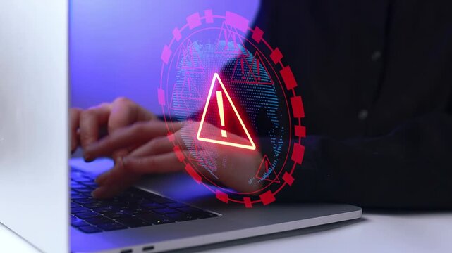 Person uses laptop while alert symbol shows on screen during a work session in an office setting.