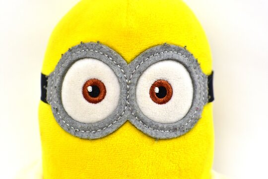 Close-up of Minion plush toy eyes and goggles isolated on white background. Detailed fabric texture and embroidered features, macro studio photography of popular cartoon character.