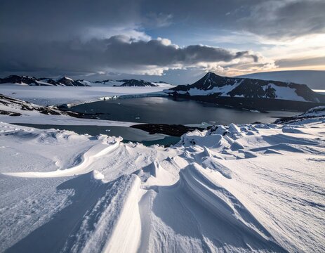 Snowy, windswept landscape with a dark, calm body of water.
