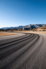 Empty Race Track Curve with Distant Mountains Under Clear Blue Sky