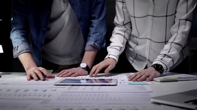 Business professionals analyzing financial data with charts and graphs on a tablet and paper, collaborating on market strategy and corporate growth planning in an office setting