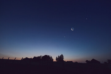 Morning old Moon with stars, planets and rural countryside tree silhouettes.
