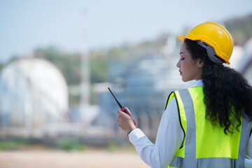 portrait of a female worker. female construction worker. person in helmet using radio communication. person in helmet with oil tanks in the desert on background.	