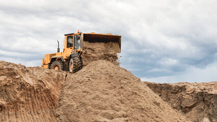 Obraz premium A powerful loader expertly shifts piles of sand, crafting a new terrain as dark clouds loom above, signaling a potentially stormy day at the bustling site