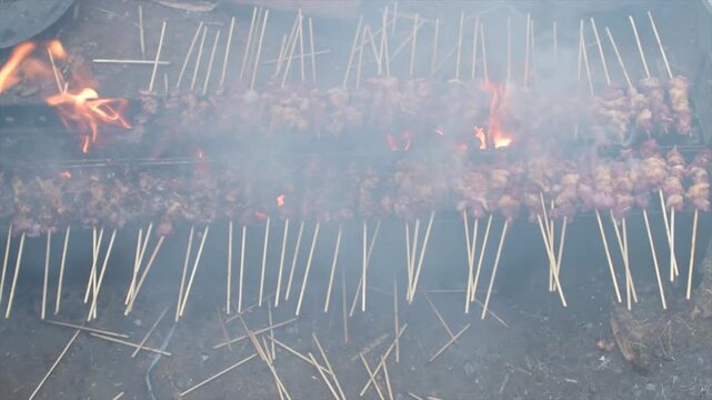 Authentic Indonesian beef satay grilling over traditional charcoal fire with smoke in 4K.
