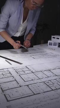 Architect designing building plans on blueprints using a compass, creating residential construction project layout. Architecture and business concept in low key lighting