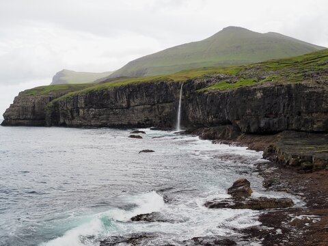 Green nordic landscapes of the Faroe Islands. Molin waterfall flowing down from cliffs into the Atlantic Ocean amidst greenery, Eysturoy island.