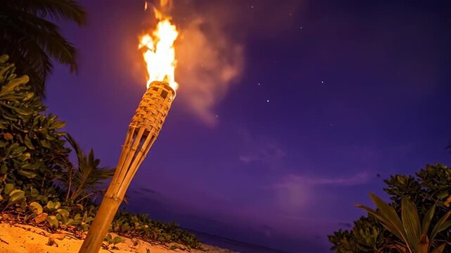 Dramatic bamboo tiki torch burning on a tropical beach at twilight.