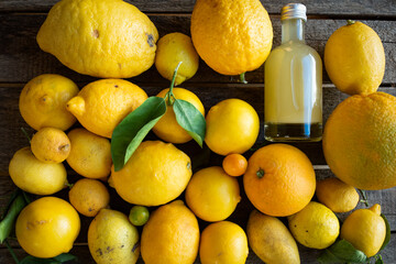 Various lemons with small bottle of limoncello liqueur on dark vintage wood. Close-up from above.